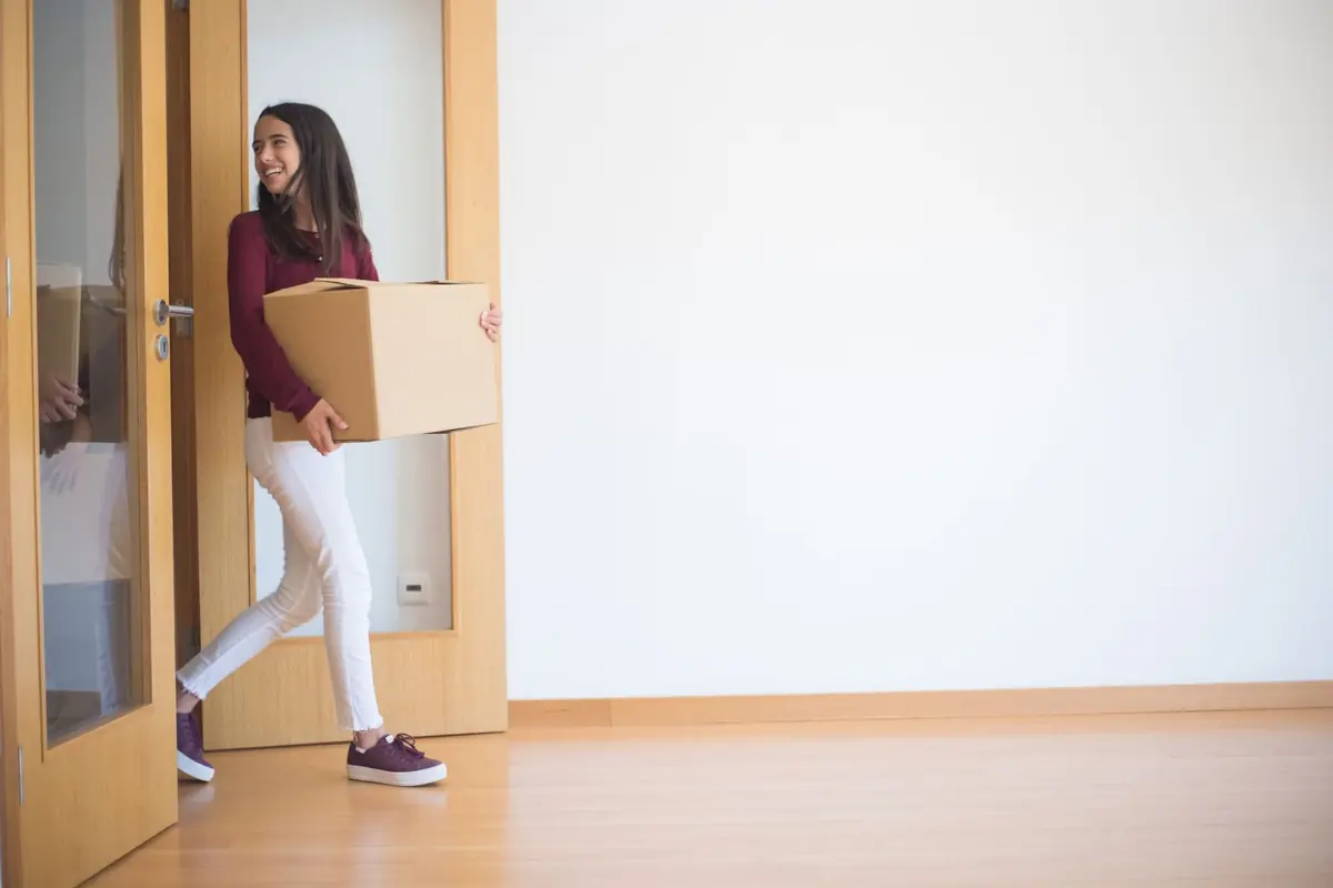 Eine Frau trägt einen Umzugskarton durch eine Wohnungstür