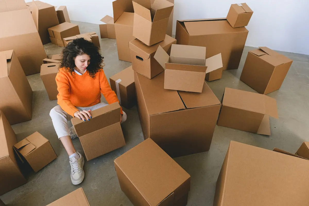 Eine Frau sitzt beim Packen zwischen zahlreichen Umzugskartons