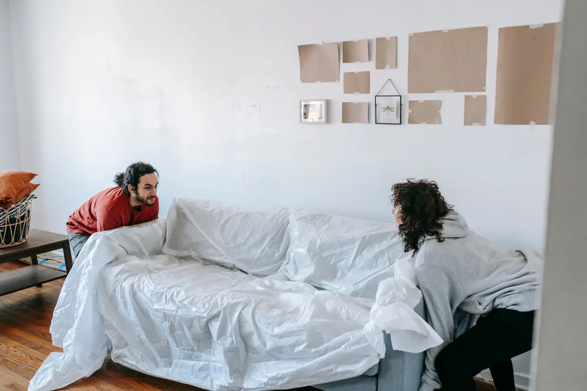 Zwei Personen decken ein Sofa für den Umzug ab