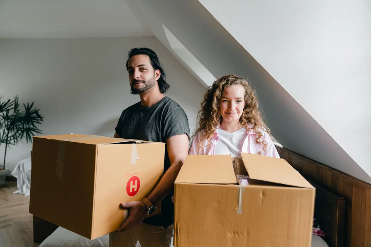 Zwei Personen tragen Umzugskartons unter einer Dachschräge